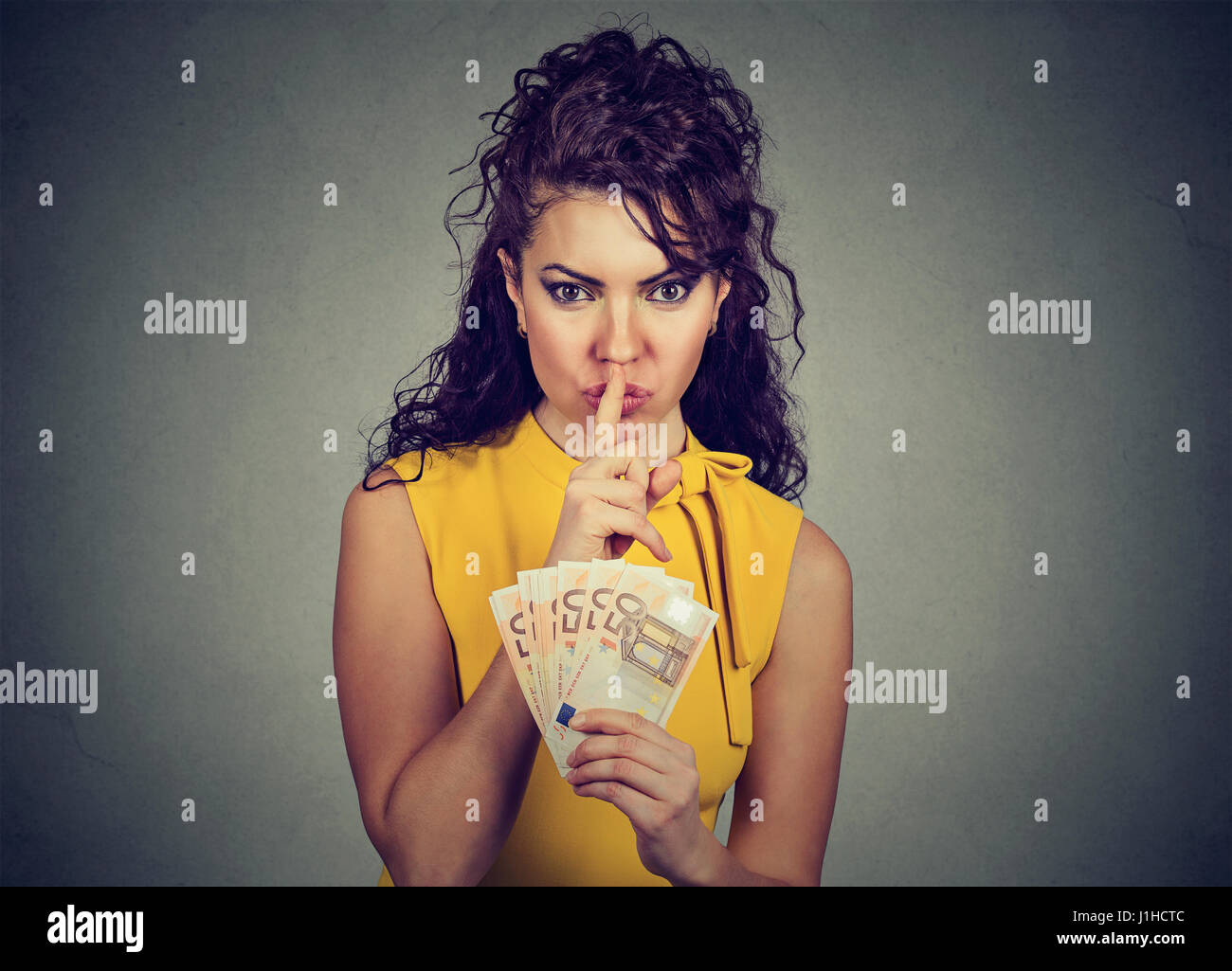 Corrupt, secretive woman with euro money showing shhh sign, isolated on gray background. Bribery concept in politics Stock Photo