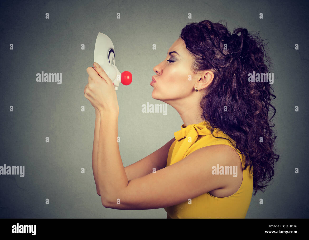 Woman kissing clown mask isolated on gray wall background Stock Photo