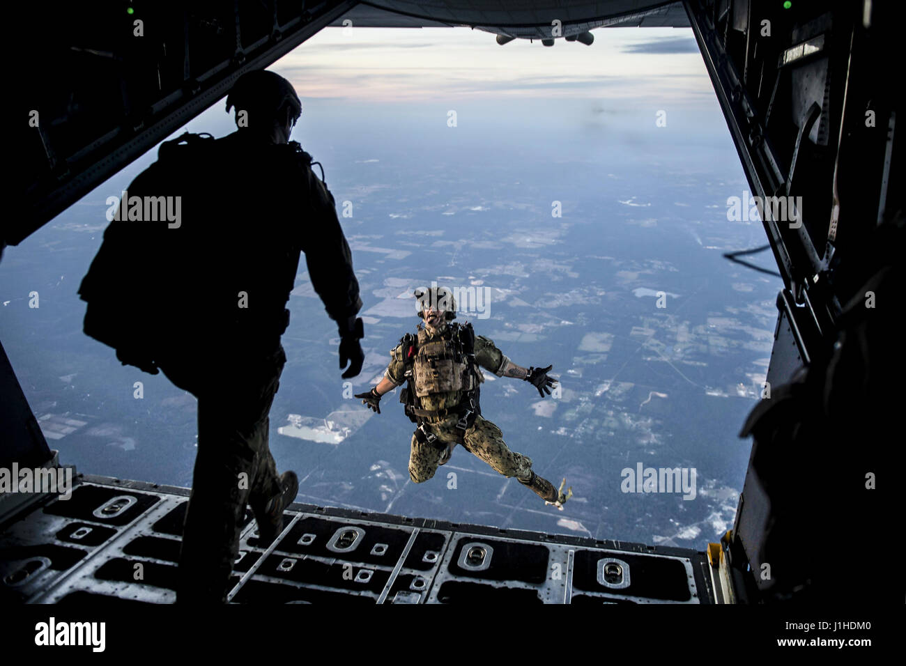 A Naval Warfare service member leaps from an Air Force MC-130 Combat Talon II during a high-altitude, low-opening jump Stock Photo