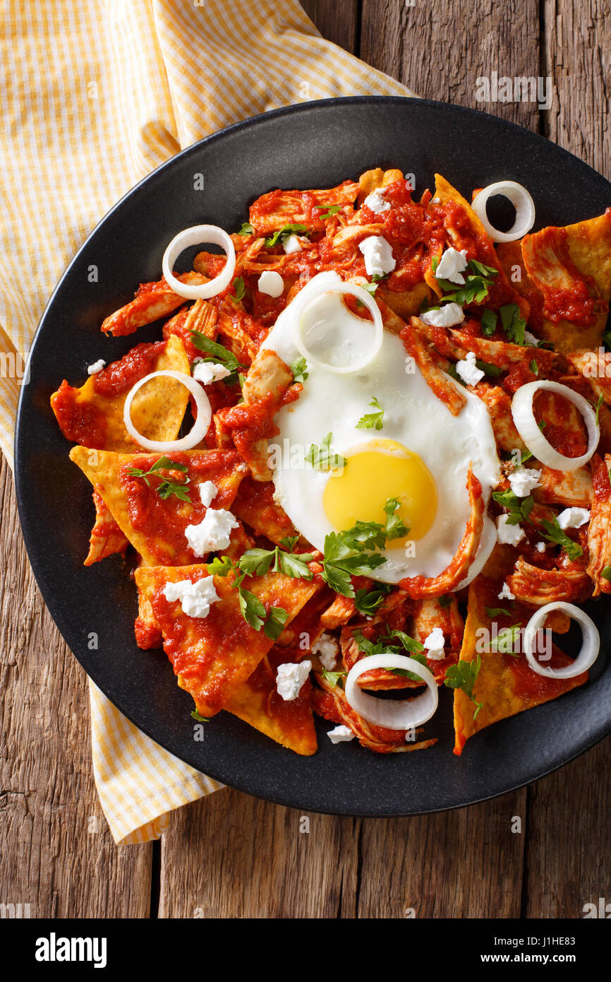 Mexican breakfast: chilaquiles with egg and chicken close-up on a plate. Vertical view from above Stock Photo