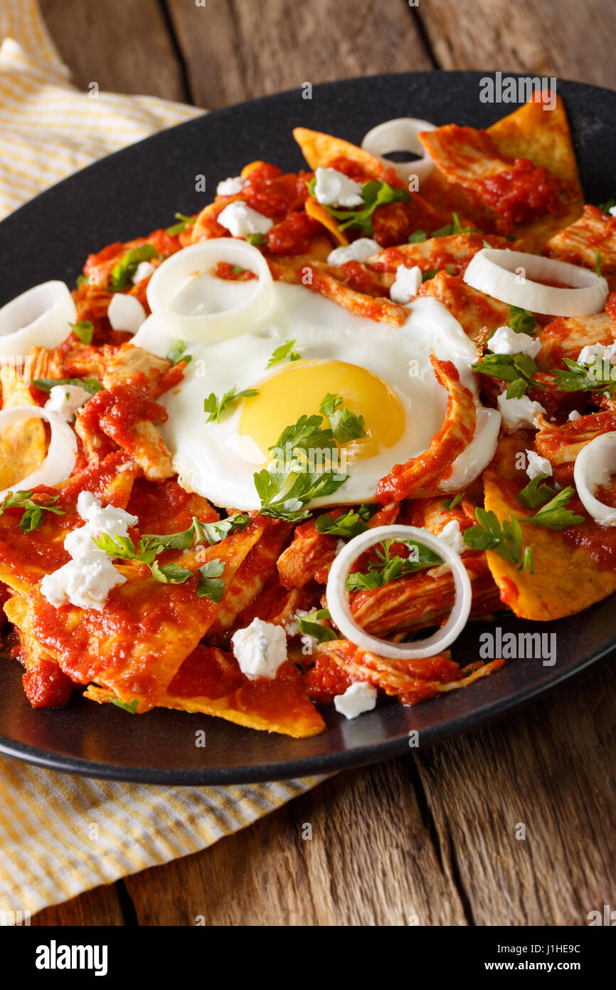 Mexican breakfast: chilaquiles with egg and chicken close-up on a plate. Vertical Stock Photo