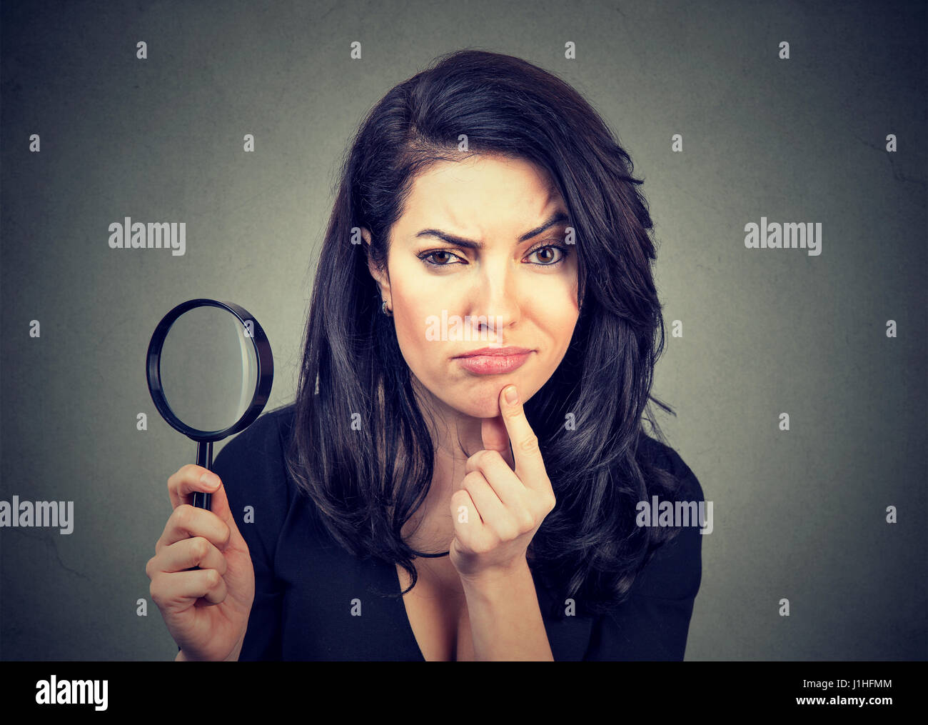Curious young woman with magnifying glass isolated on gray wall background. Stock Photo