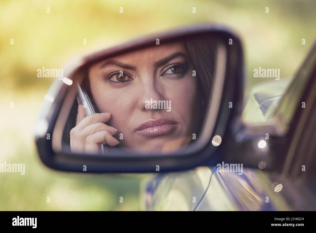 Young woman driving in car and talking on her phone, annoyed by conversation or bad voice message, outdoors background Stock Photo