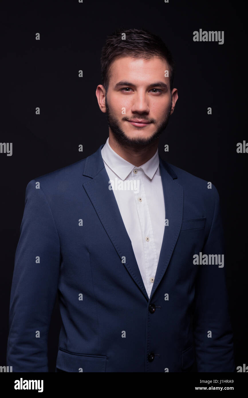 young adult man, 20s smirking, good looking, white shirt, elegant suit jacket, black background studio Stock Photo