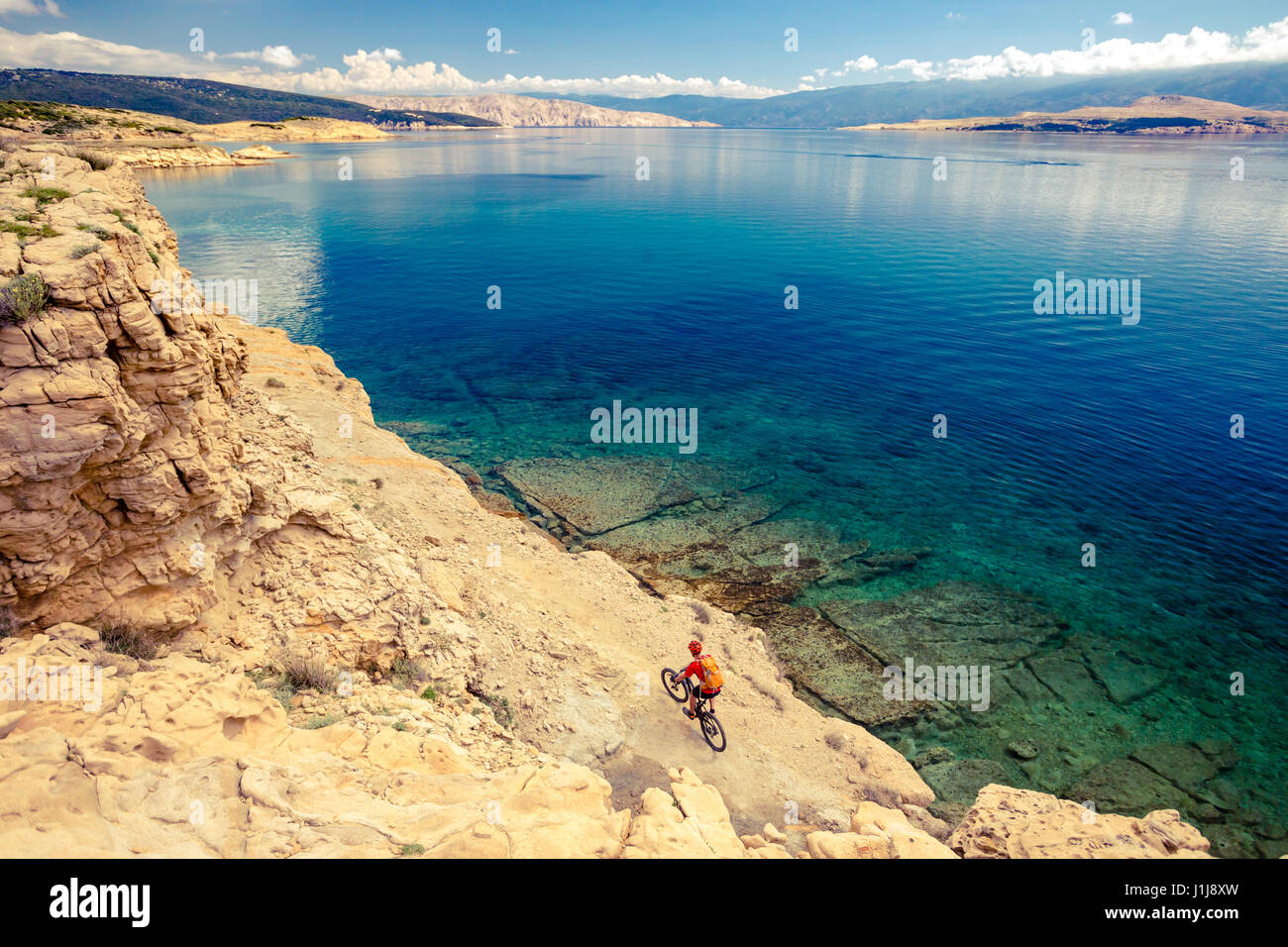 Mountain biker riding on bike in summer inspirational mountains and sea landscape. Man cycling MTB on enduro trail track at seaside and rocky dirt pat Stock Photo