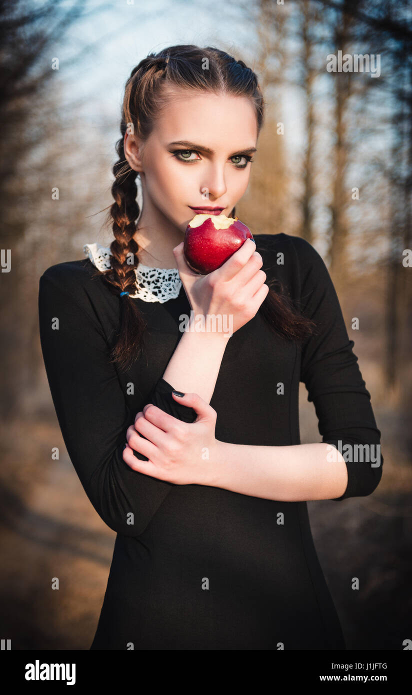Outdoor portrait of a cute young girl in old-fashioned dress eating red apple Stock Photo
