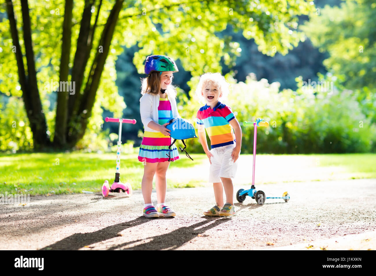Children learn to ride scooter in a park on summer day. Preschooler