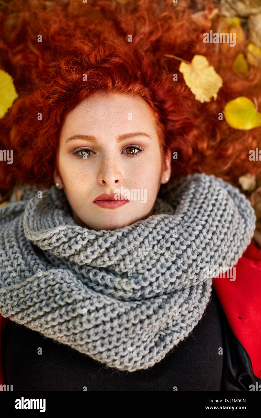 Portrait of red haired woman lying on fallen leaves, top view Stock Photo