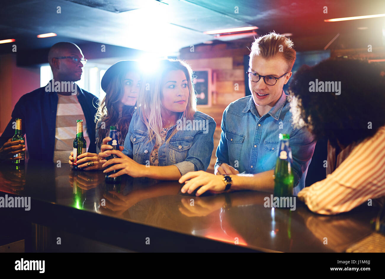 Young friendly people sitting at the bar counter with the beer. Horizontal indoors shot. Stock Photo