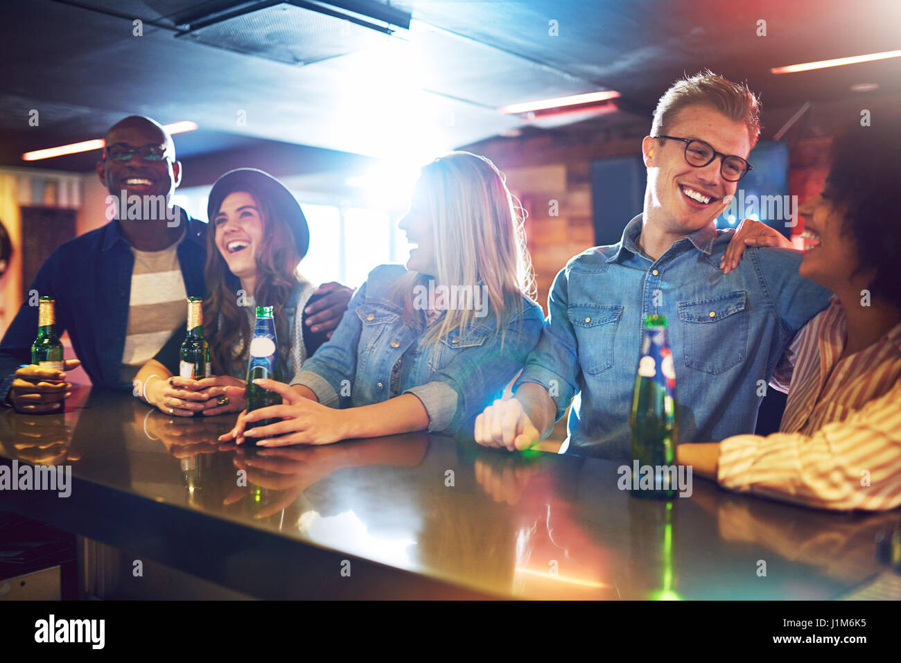 Sitting at the bar counter friends laughing and talking to each other while having a beer. Stock Photo