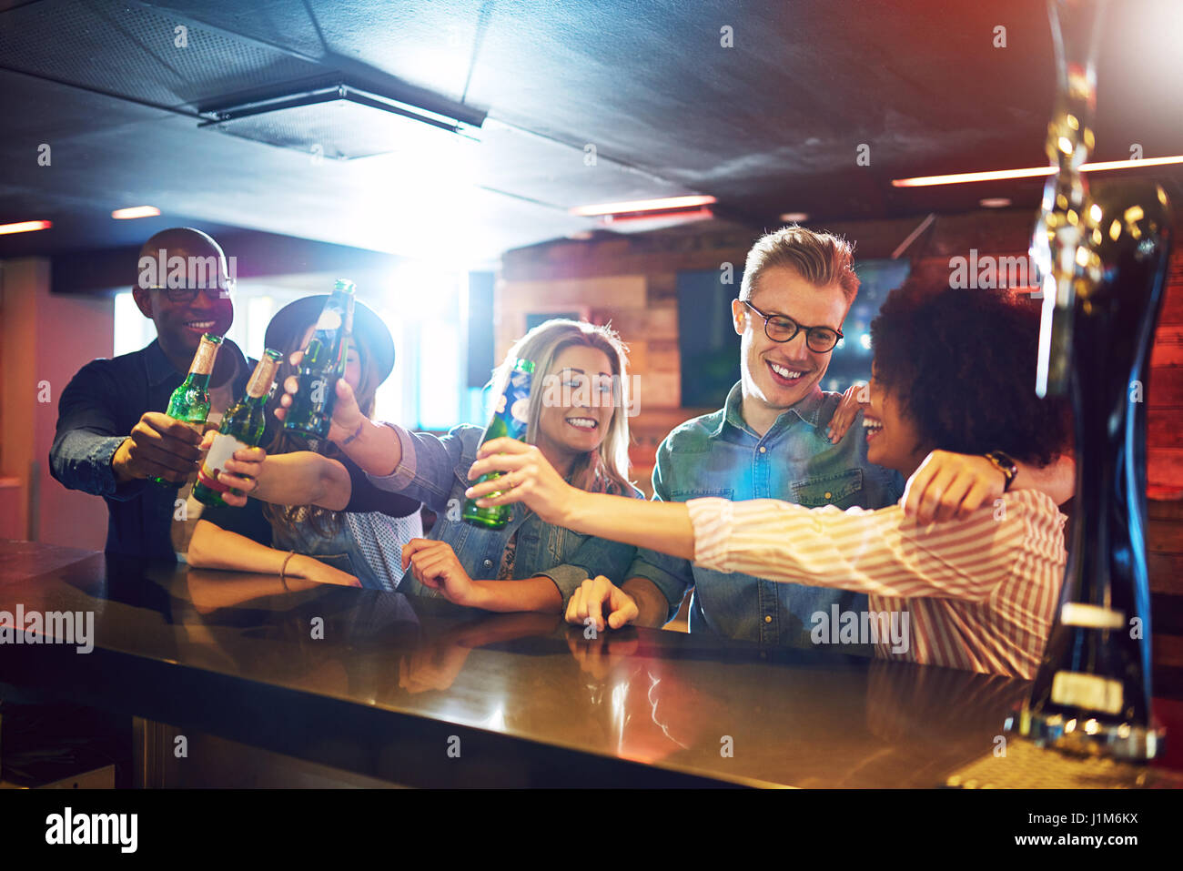 Horizontal shot of people with beer showing cheers gesture at the bar counter. Stock Photo