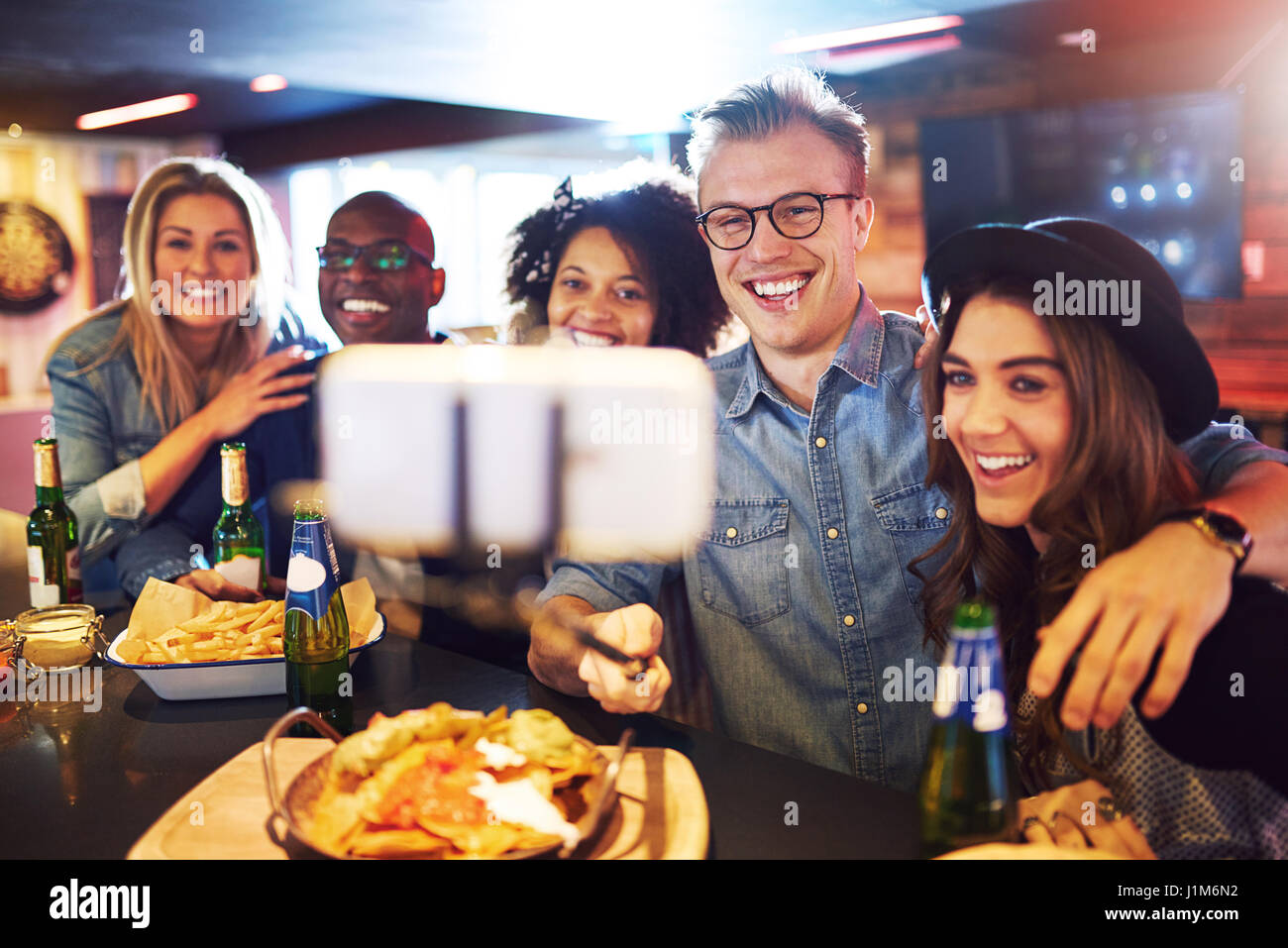 Horizontal shot of smiling people taking a selfie on the smartphone inside the bar. Stock Photo