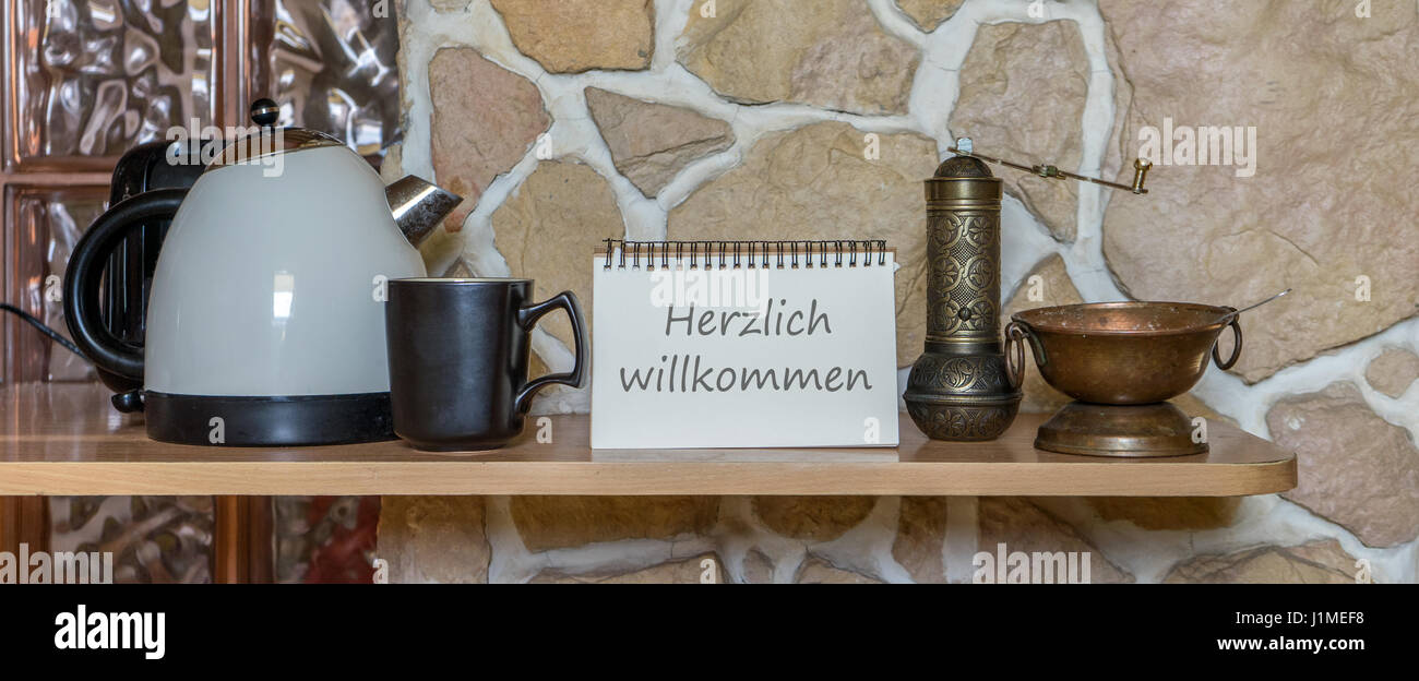 Water cooker, cup and notepad with german text Welcome Stock Photo