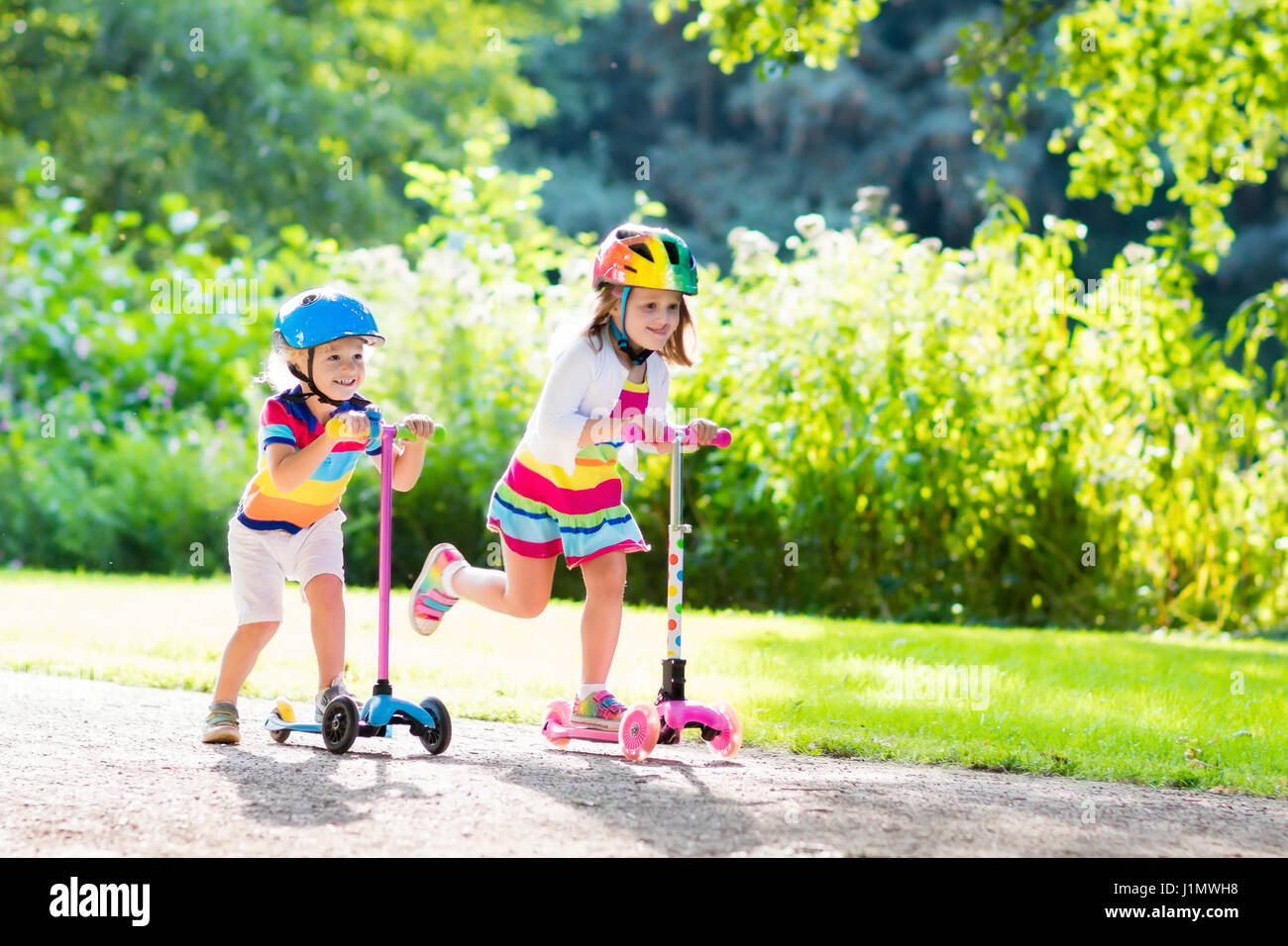Children learn to ride scooter in a park on sunny summer day. Preschooler  boy and girl in safety helmet riding a roller. Kids play outdoors with  scoot Stock Photo - Alamy