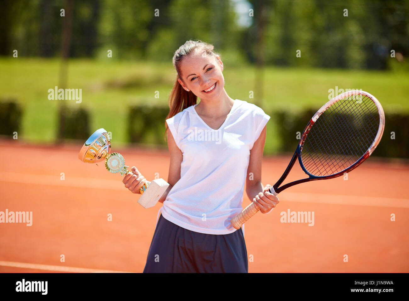 Young female winner in tennis match holding goblet on tennis court Stock Photo