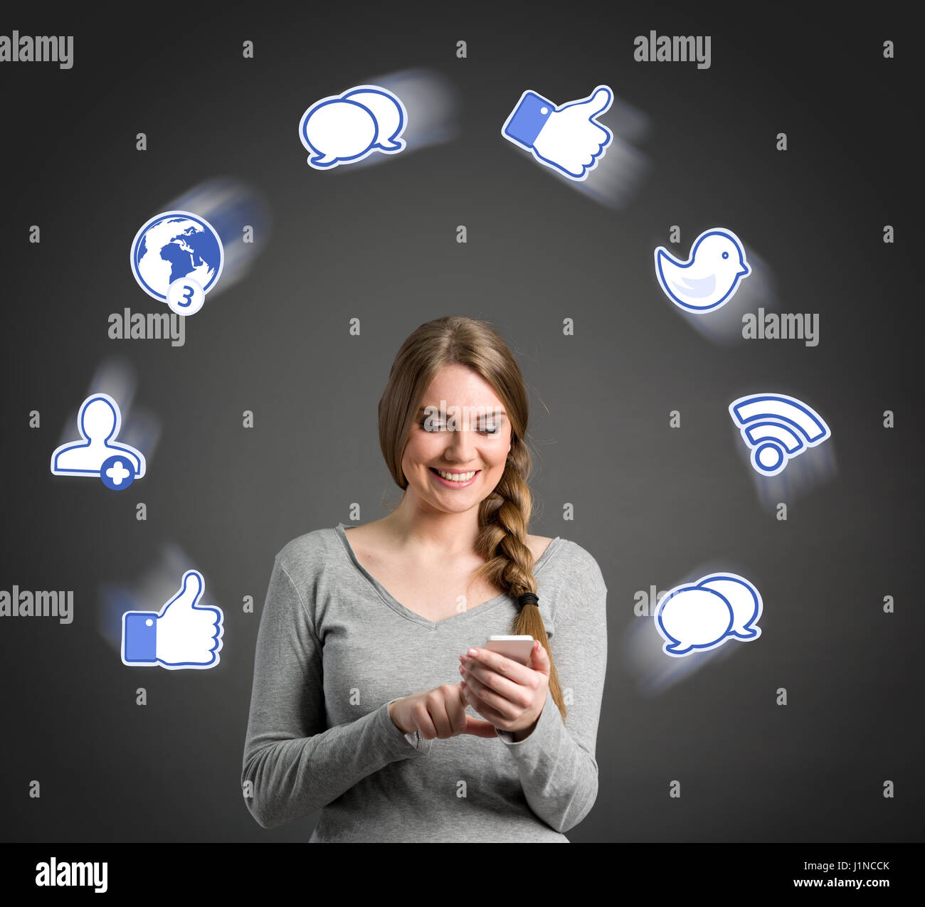 Smiling young woman using smart phone with illustrated media social icons around her Stock Photo
