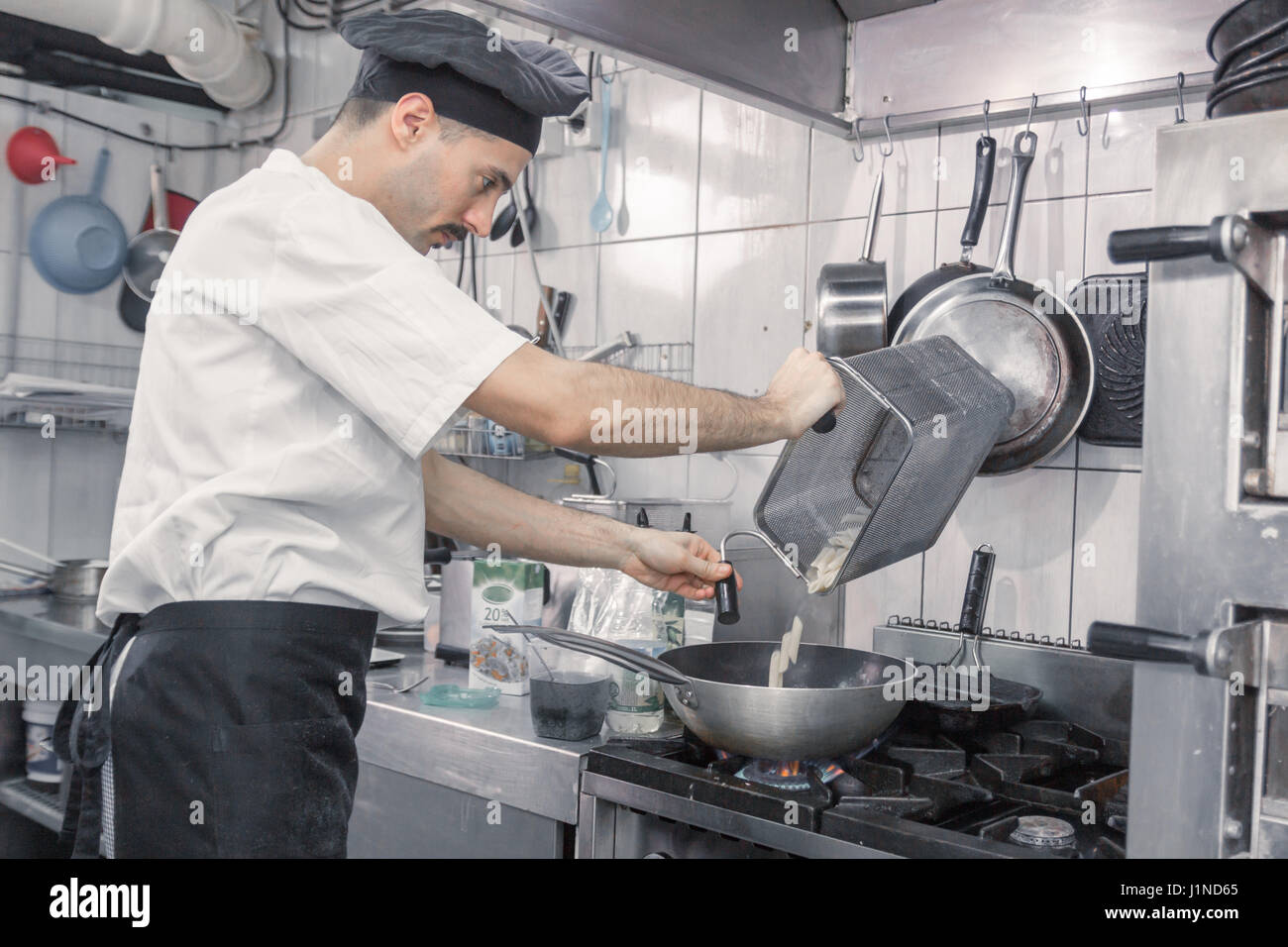 young adult man, professional chef transferring pasta pan, commercial kitchen Stock Photo