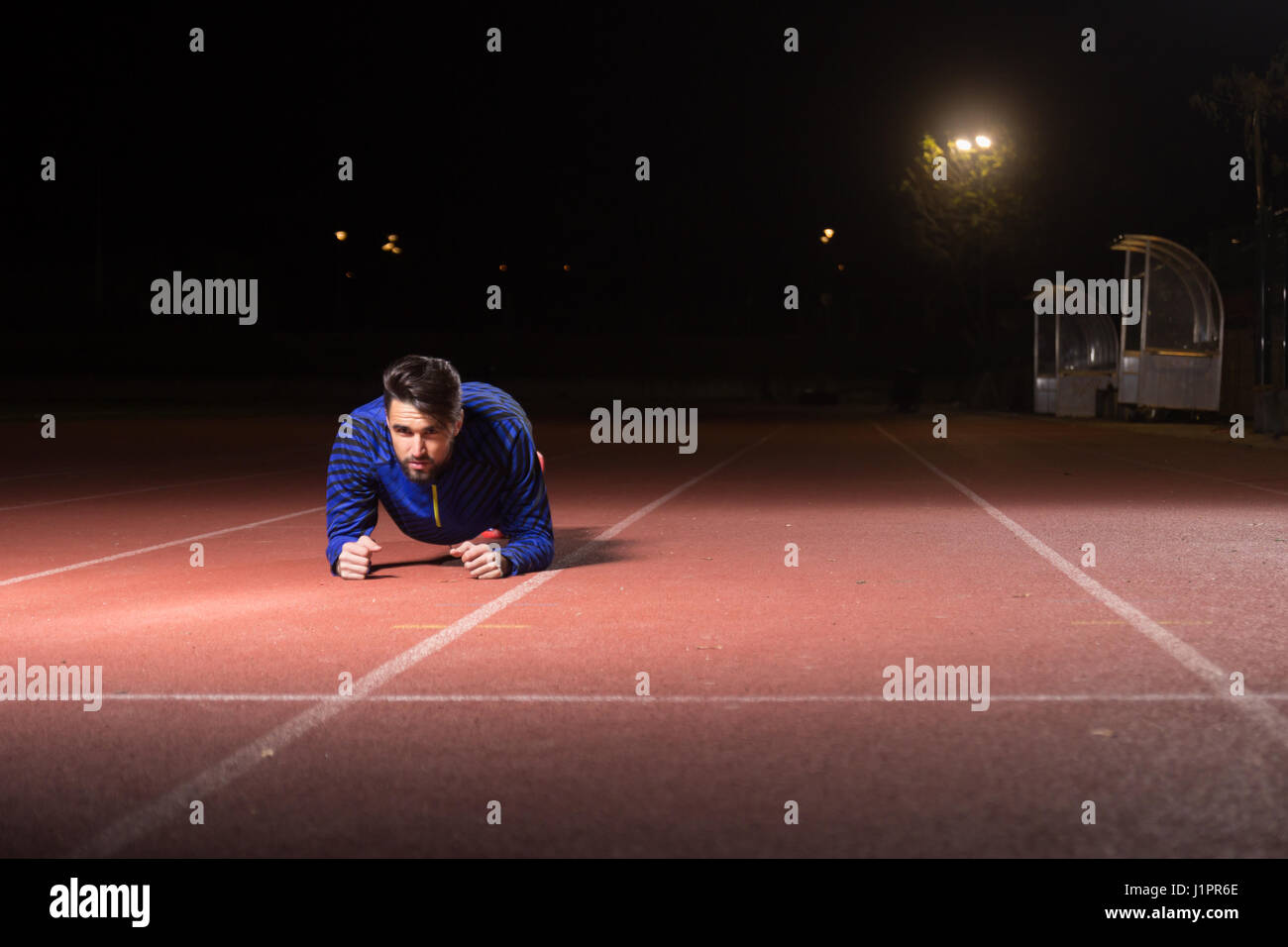 Young adult man, athlete plank exercise, night. Red running tracks ...