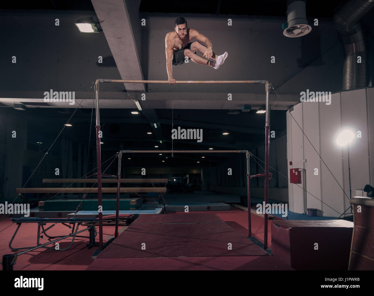 young adult man gymnast, gymnastic horizontal bar, in air. Dark hall