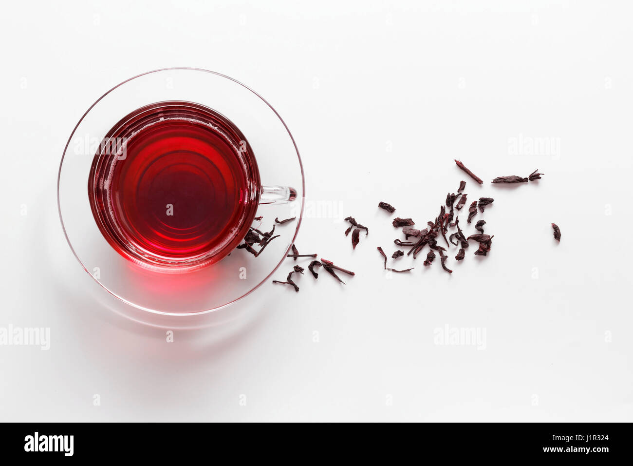 transparent glass cup with Hibiscus tea on the saucer with dry tea leaves on a white background Stock Photo