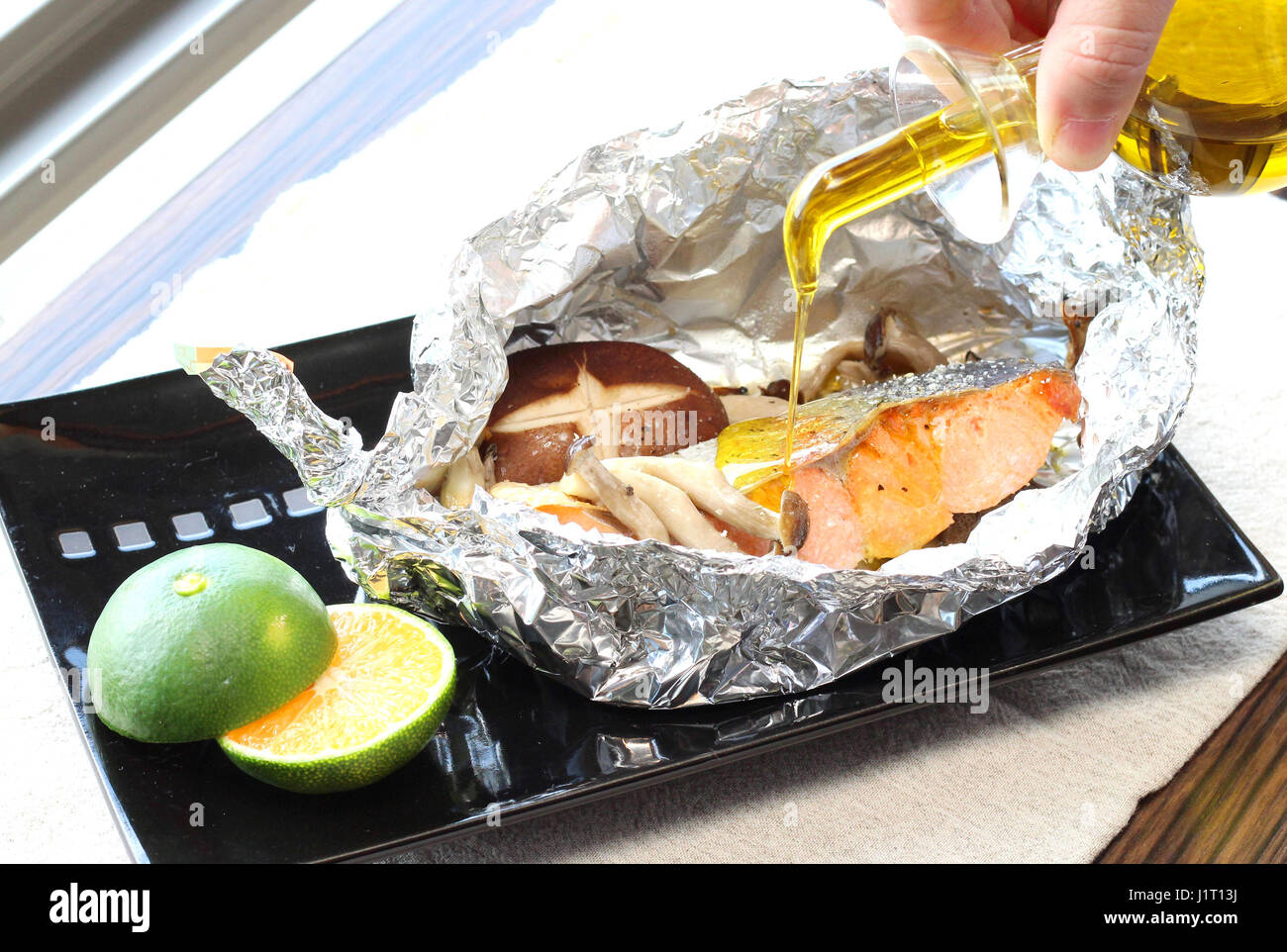 Mixing cod fillet with mushroom in foil for grilling on black platter with lemon Stock Photo