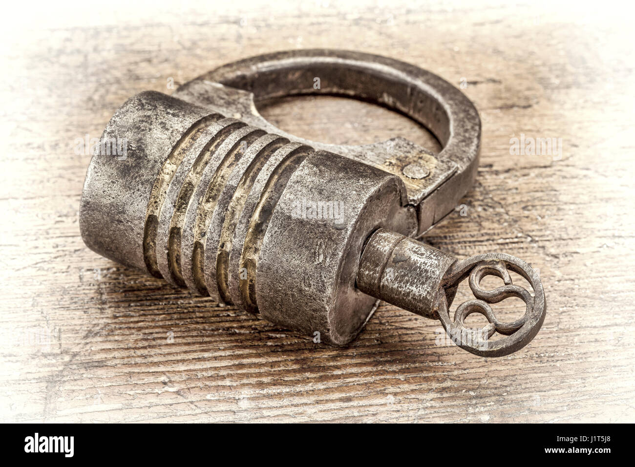 Vintage round shape hand crafted screw type iron padlock with a key on rustic wood, retro sepia toning Stock Photo