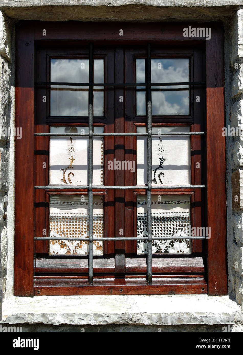 Wooden window with elegant curtains, sky reflection and steel bars on