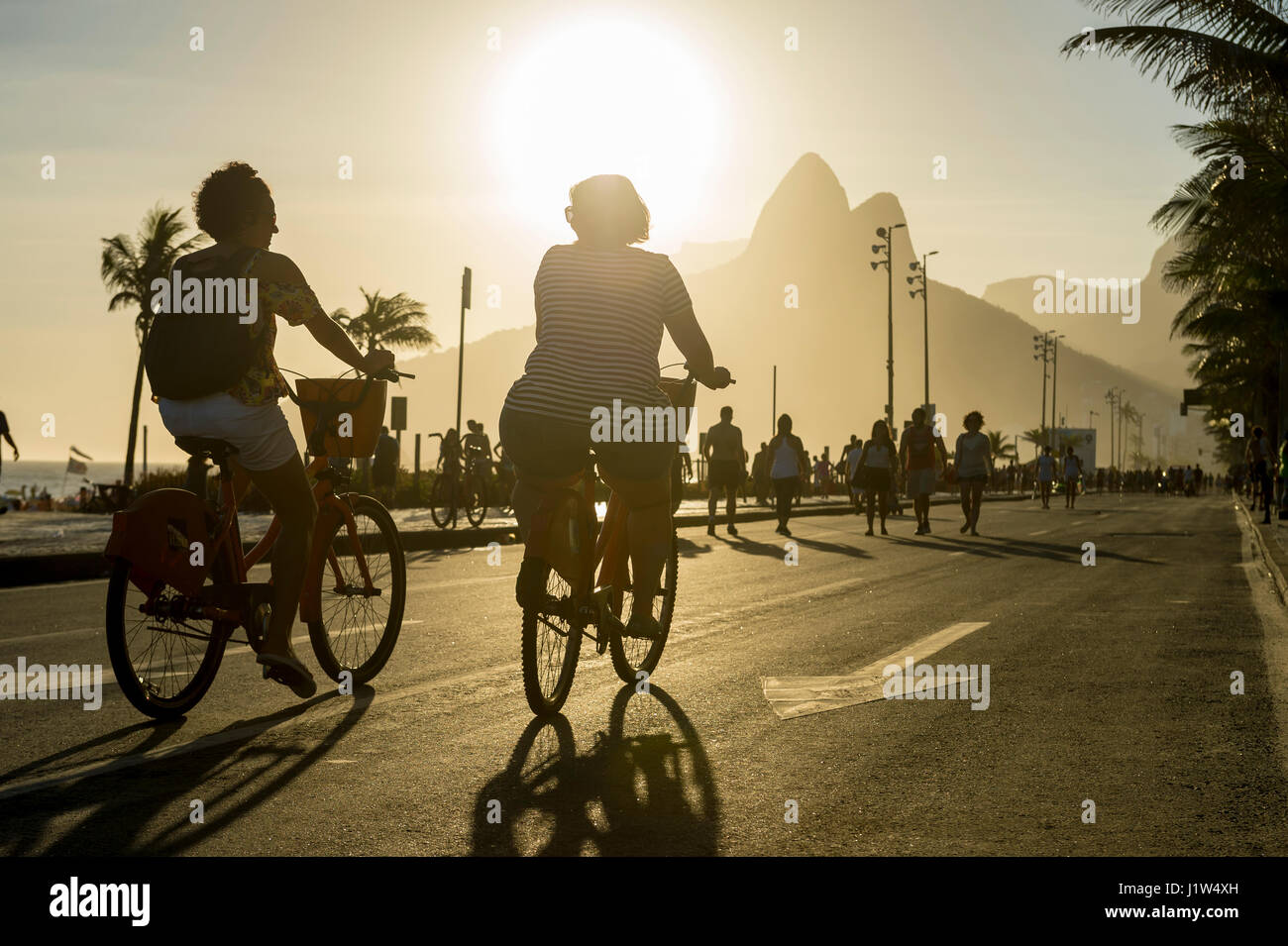 RIO DE JANEIRO - FEBRUARY 12, 2017: Pair of cyclists pass in front of the sunset view of Ipanema Beach on a traffic-free Sunday afternoon. Stock Photo