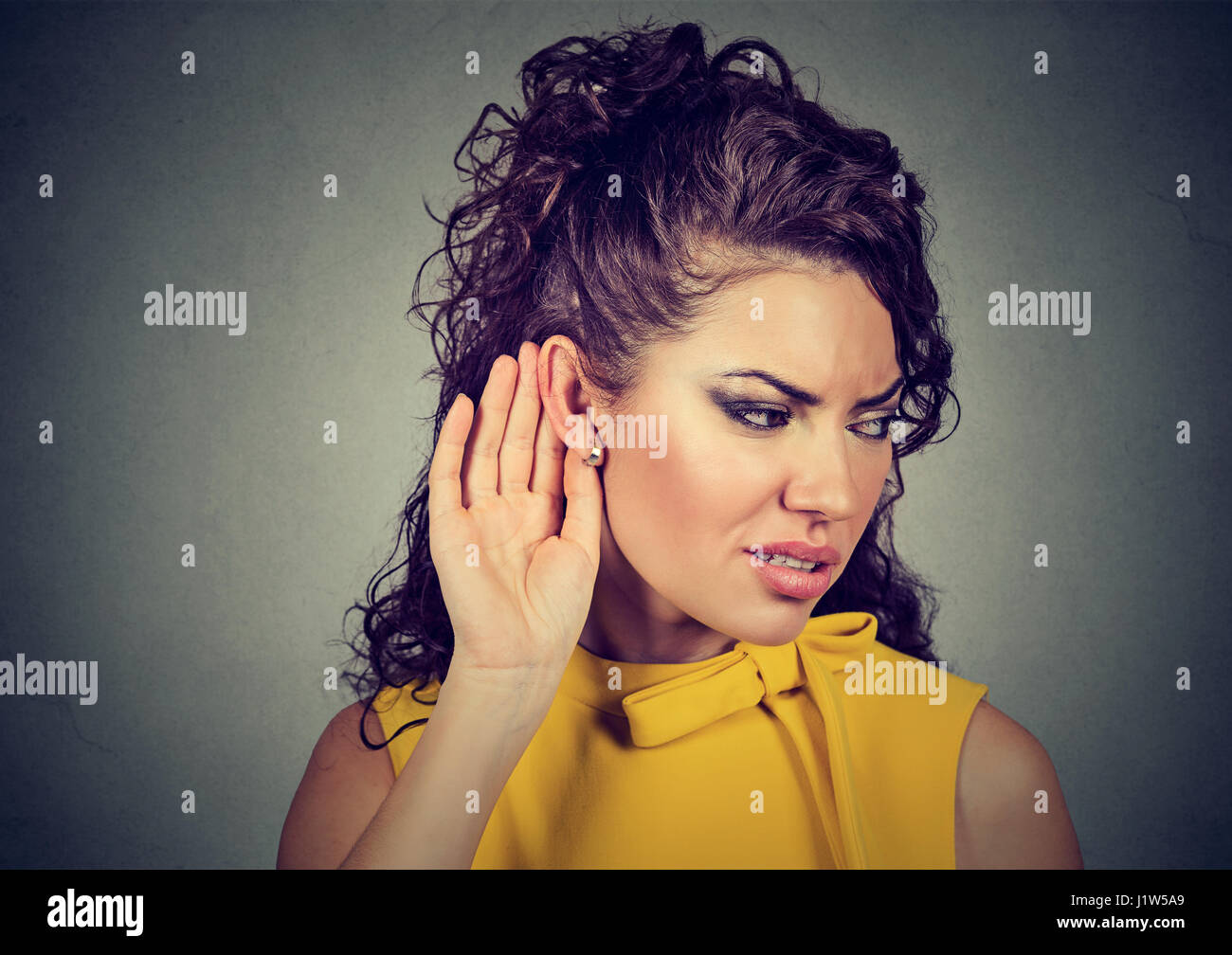 Curious worried woman with hand to ear carefully listening to gossip conversation isolated on gray background Stock Photo
