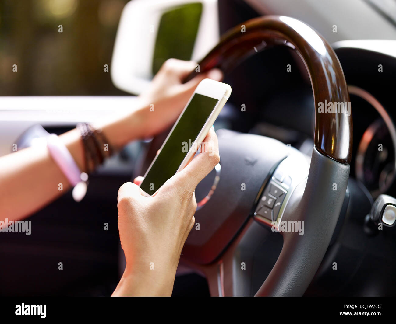 hands of female holding cellphone and steering wheel inside a vehicle. Stock Photo