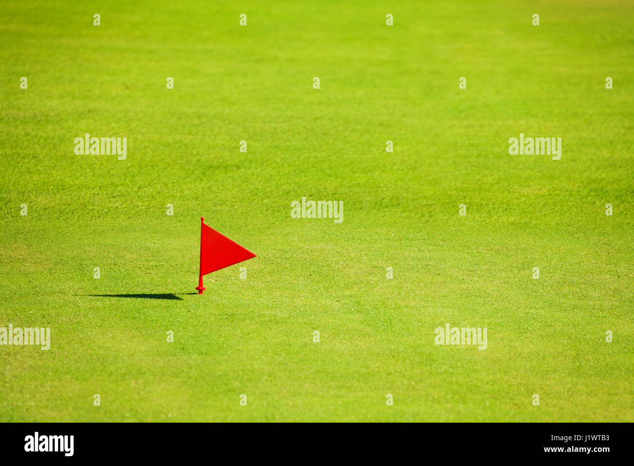 Putting green with red flag marker at end of fairway on the golf course
