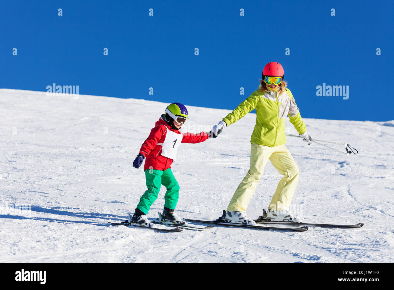 Portrait of active mother teaching her kid son skiing holding him by hand in snowy mountains Stock Photo