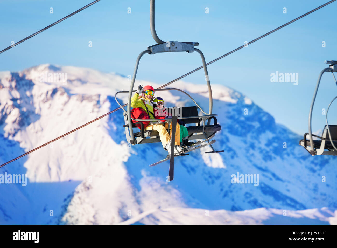 Portrait of happy young woman and her son lifting on chairlift against snowy mountains Stock Photo