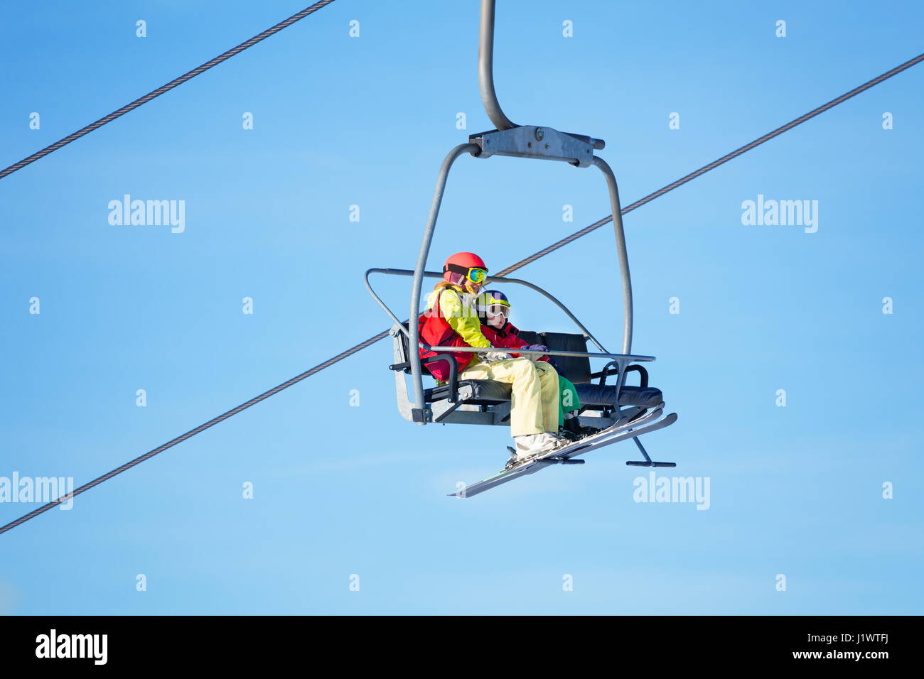 Portrait of mother with her kid son lifting on chairlift  high in the mountains against blue sky Stock Photo