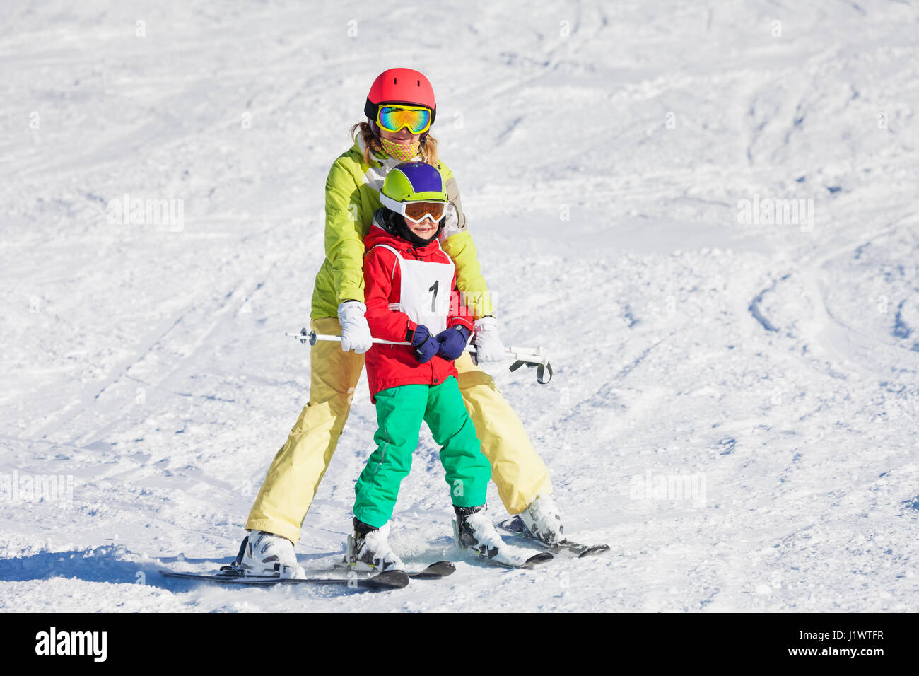 Female trainer teaching little boy skiing holding a pole and moving slowly together at sunny day Stock Photo