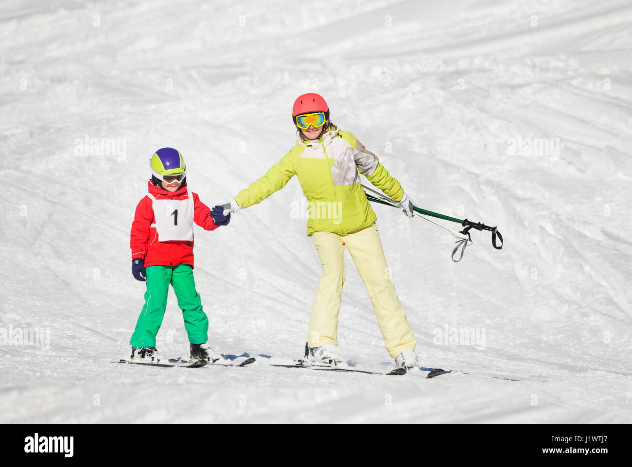 Active mother teaching her son skiing, holding hands at snowy mountains Stock Photo