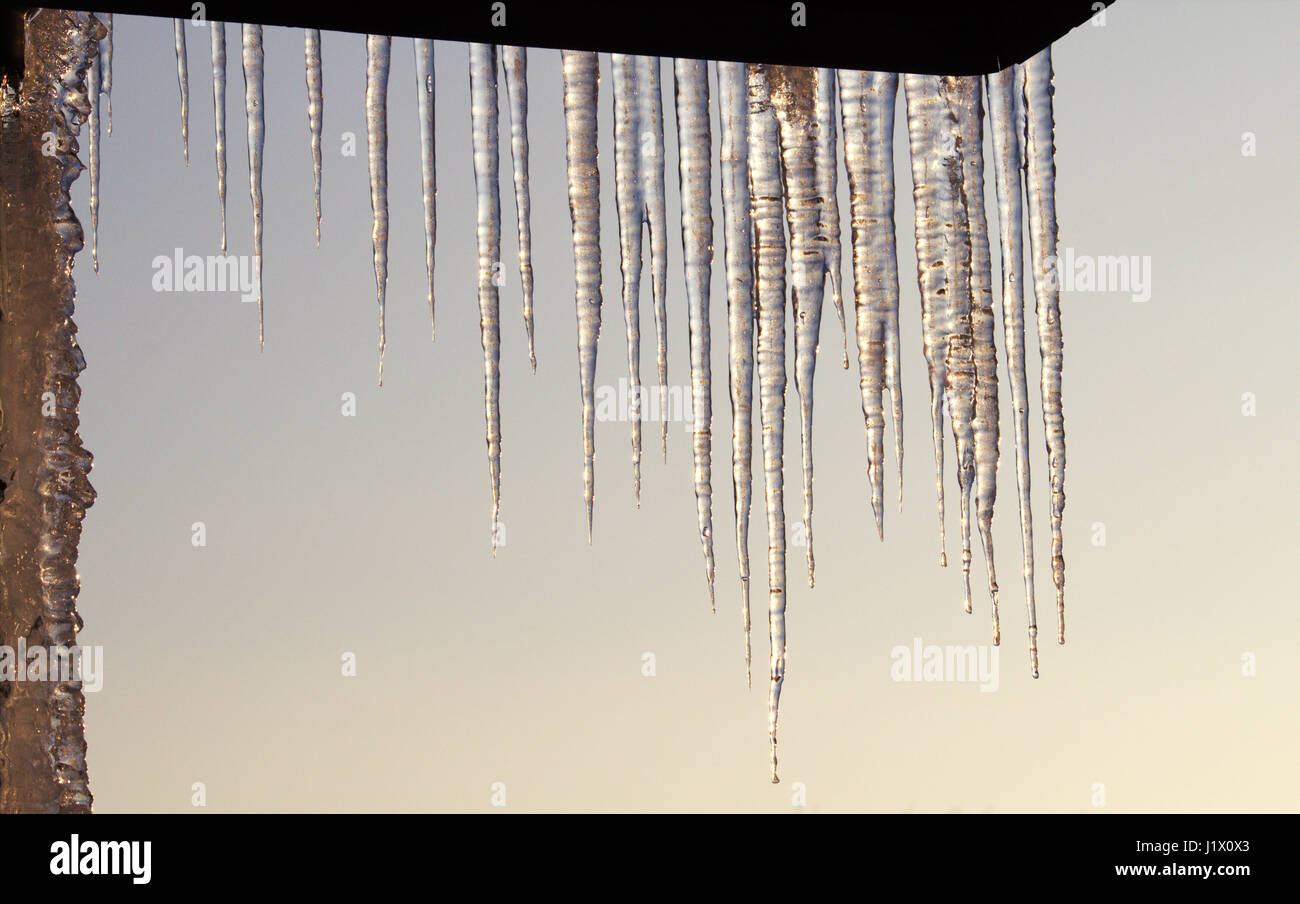 Eiszapfen hängen von einer Dachkante (gegen milchig-blauen Himmel); ice cones hanging from edge of roof Stock Photo