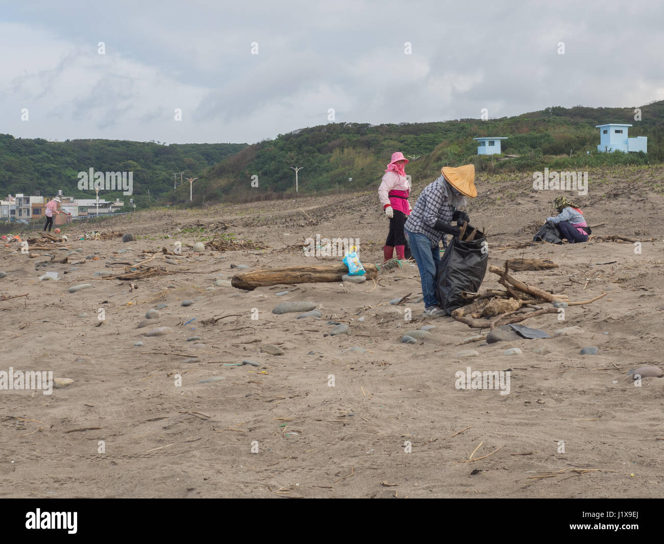Shimen, Taiwan - October 03, 2016: Women in hats and masks on  faces cleaning up a beach by the ocean Stock Photo