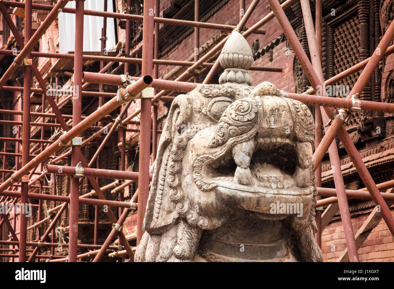 Scaffolding set up to support one of the many structures damaged in the 2015 earthquake surrounds an ornately carved statue. Durbar Square, Kathmandu. Stock Photo