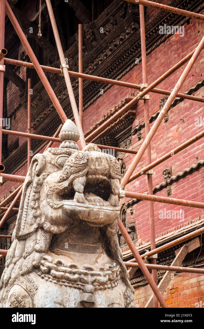 Scaffolding set up to support one of the many structures damaged in the 2015 earthquake surrounds an ornately carved statue. Durbar Square, Kathmandu. Stock Photo