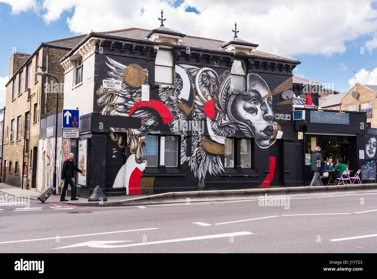 By The Bridge Cafe & Olly Studio Gallery with graffiti by street artist Caratoes and people walking in front of it. Kingsland Road, Haggerston, London Stock Photo