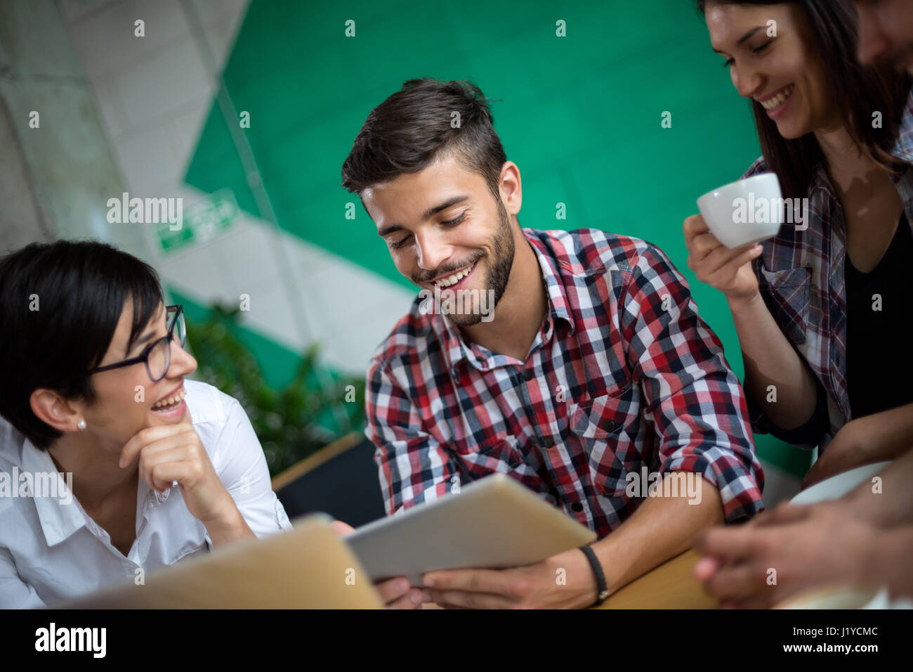Three students studying and learning in a coffee shop with a tablet