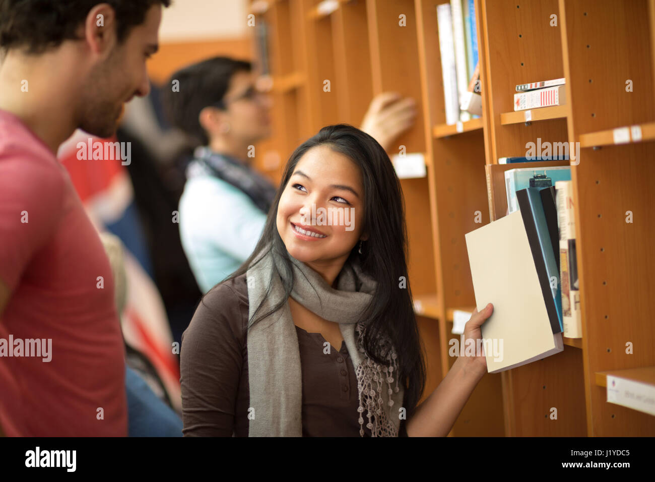 Pretty Asian student choosing books with classmate in library Stock Photo