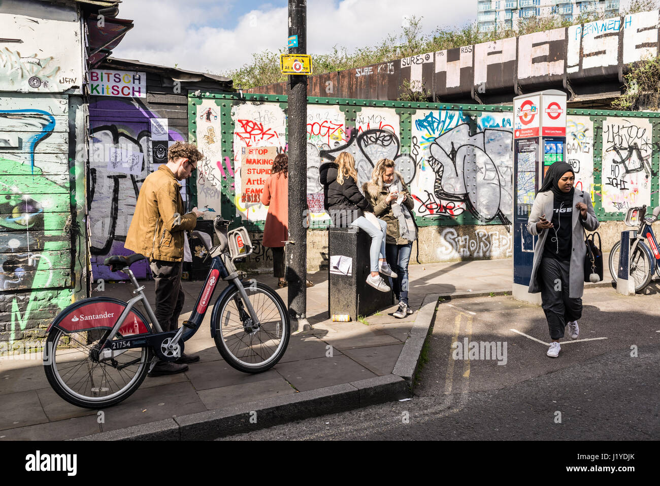 Street view of Brick lane with young hipster people walking and graffiti in background. Brick Lane, Shoreditch, London, UK Stock Photo