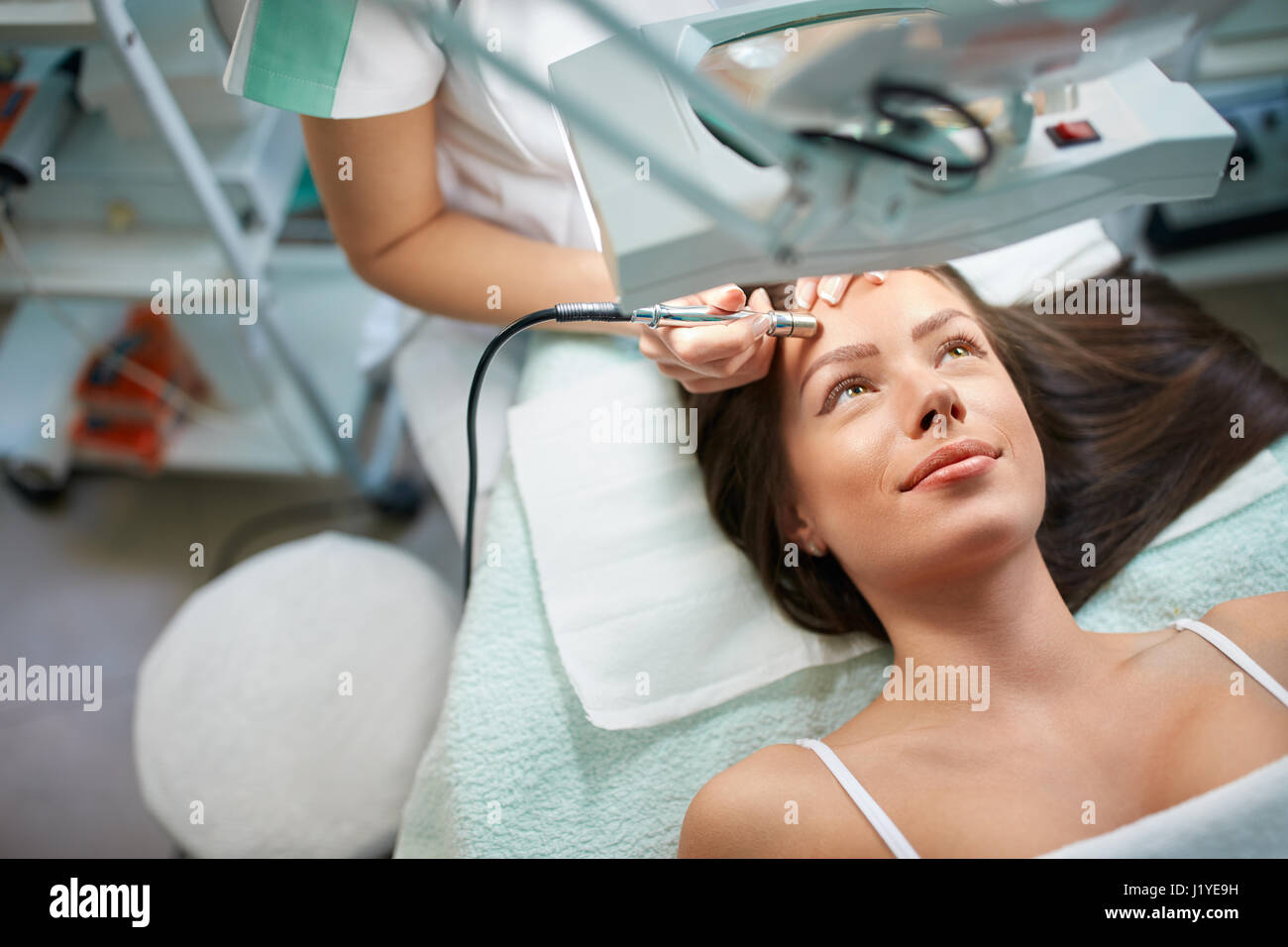Skillful cosmetologist is undergoing microdermabrasion of skin on female face Stock Photo