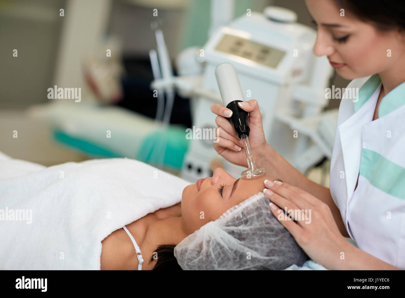 Professional cosmetologist undergoing darsonvalization on skin of face, skin and body care at beauty salon Stock Photo