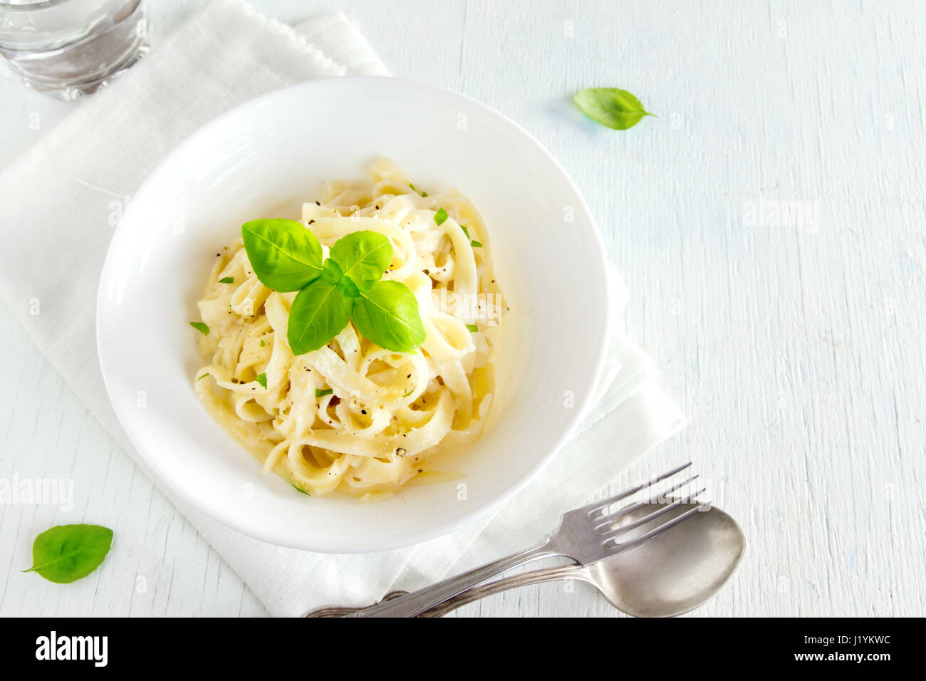 Alfredo tagliatelle pasta with basil and black pepper in white bowl