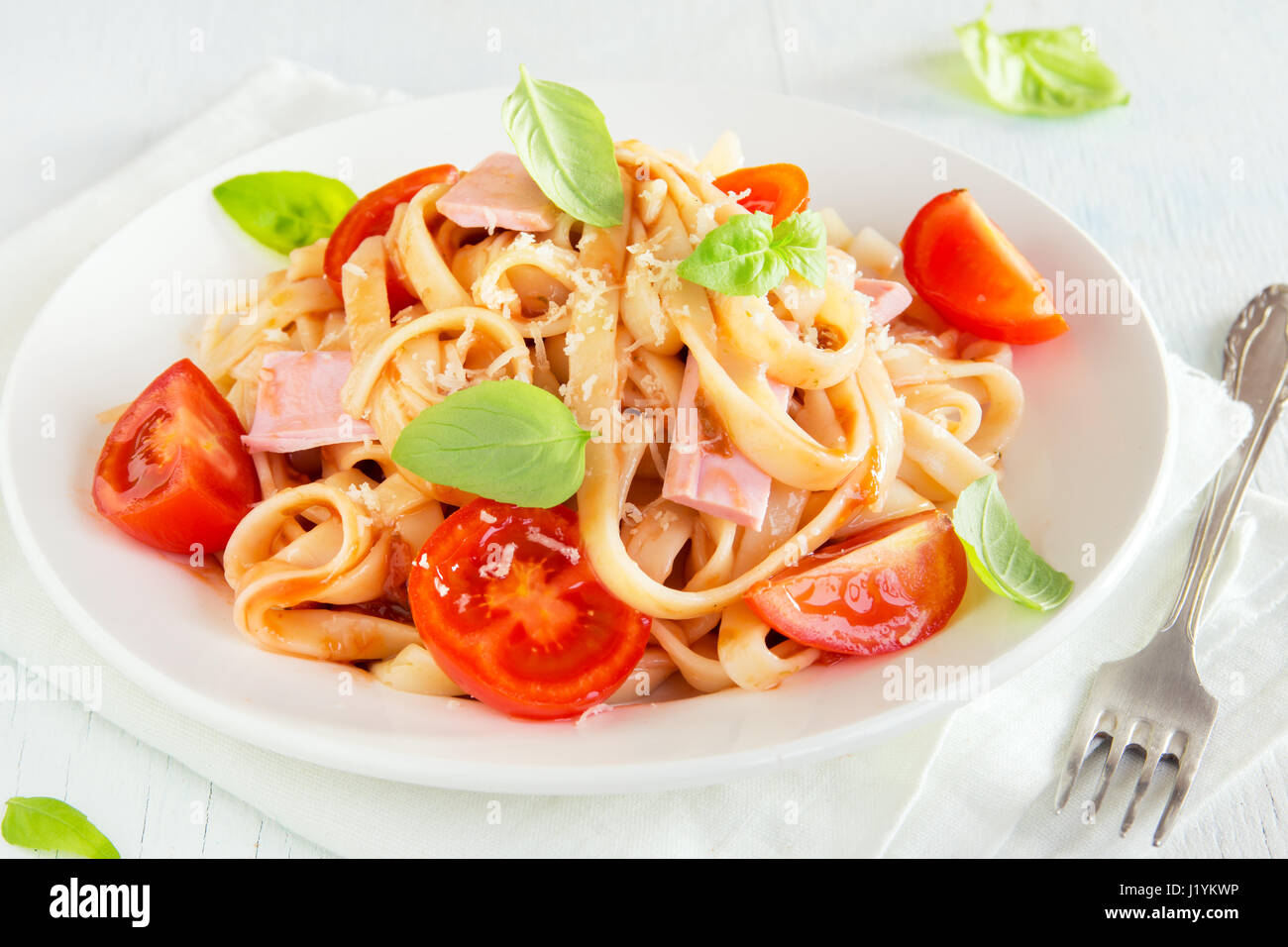Tagliatelle pasta with ham, tomato sauce, cherry tomatoes and basil