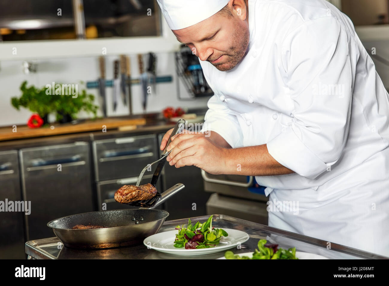 Focused chef prepares steak dish at gourmet restaurant Stock Photo