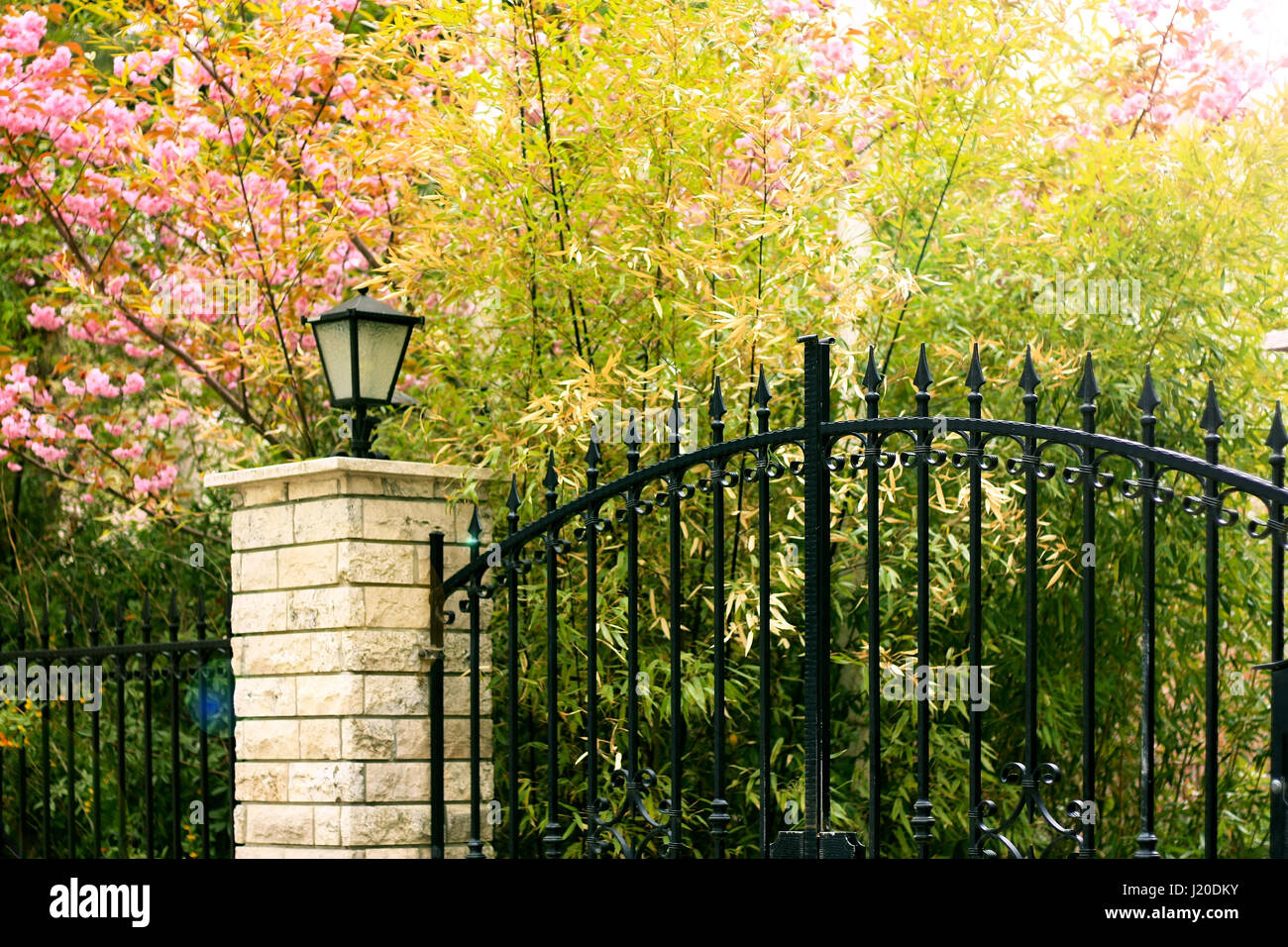 Peaceful black iron gate with colorful plants and lamp Stock Photo